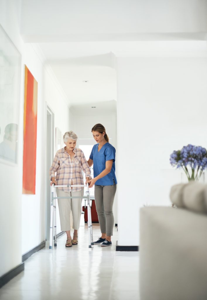 Shot of a friendly nurse helping her elderly patient to walk with a walker at home