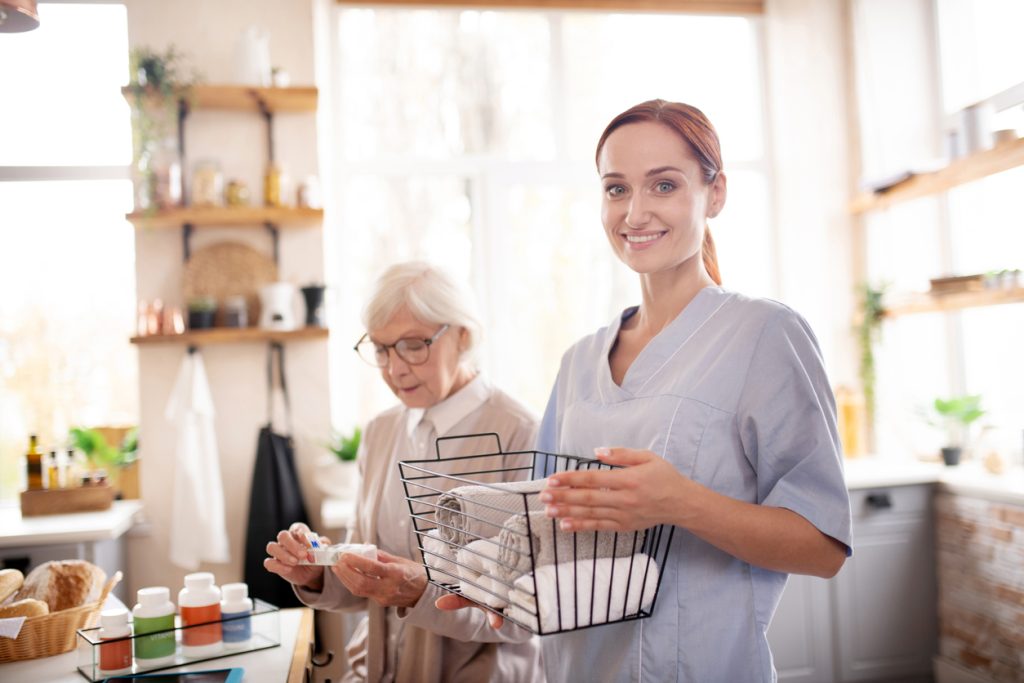 Standing near pensioner. Smiling medical attendant standing near pensioner wearing glasses